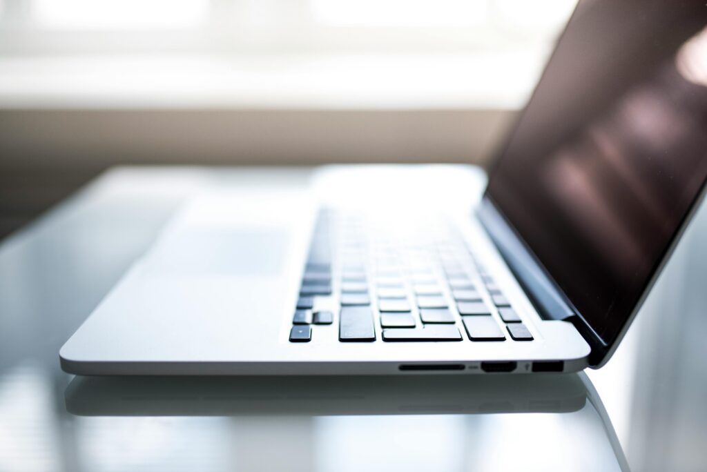 Close-up of a silver laptop on a glass desk, with the keyboard in focus and the screen tilted to the right.