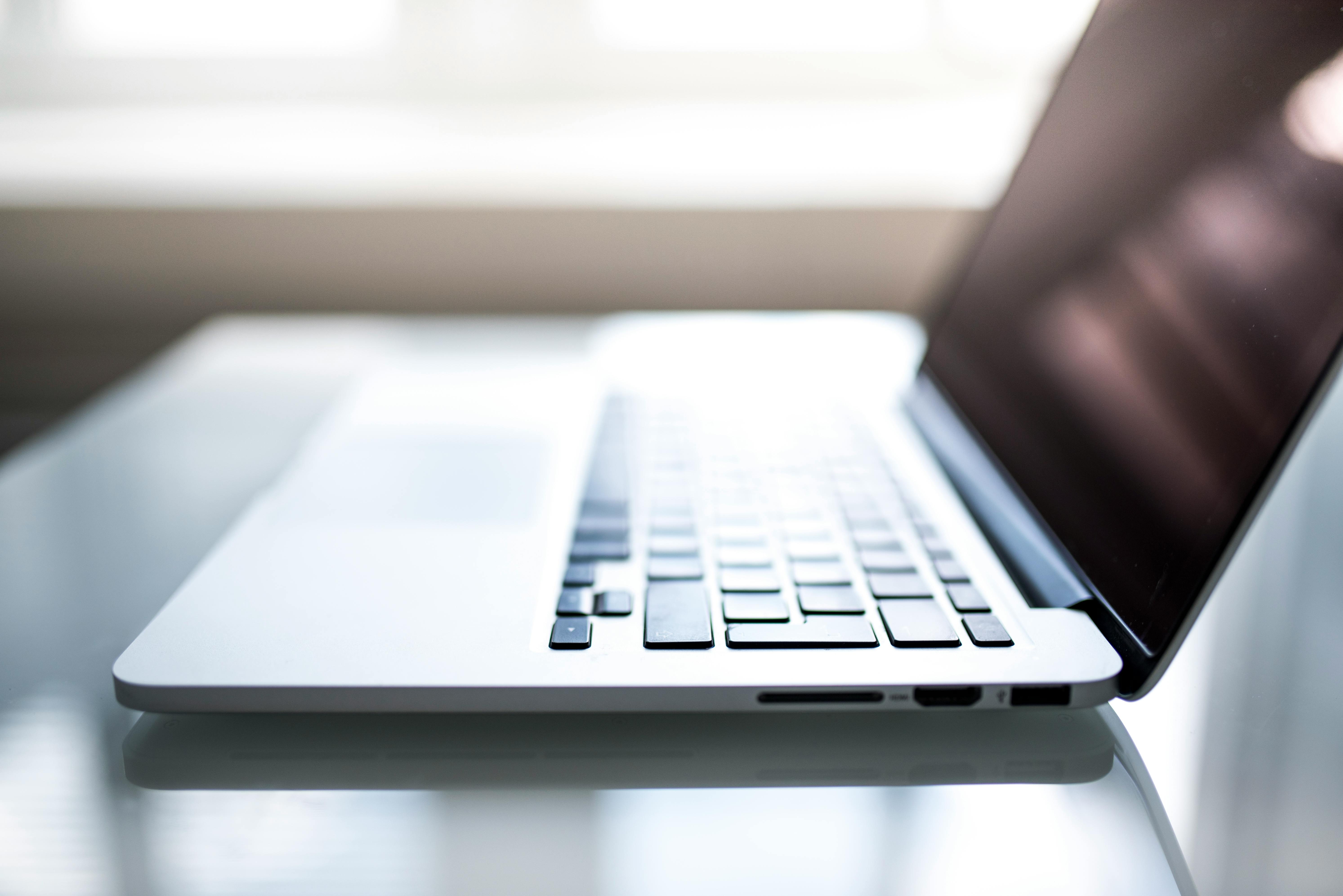 Close-up of a silver laptop on a glass desk, with the keyboard in focus and the screen tilted to the right.
