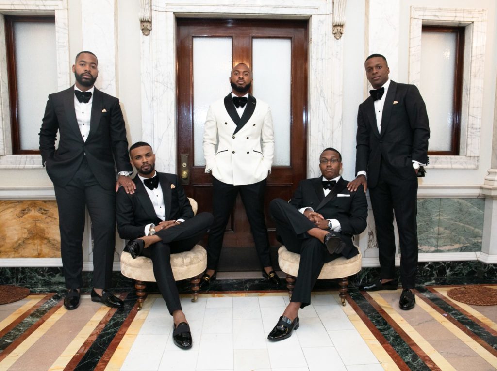 Groom and groomsmen in tuxedos in elegant hallway
