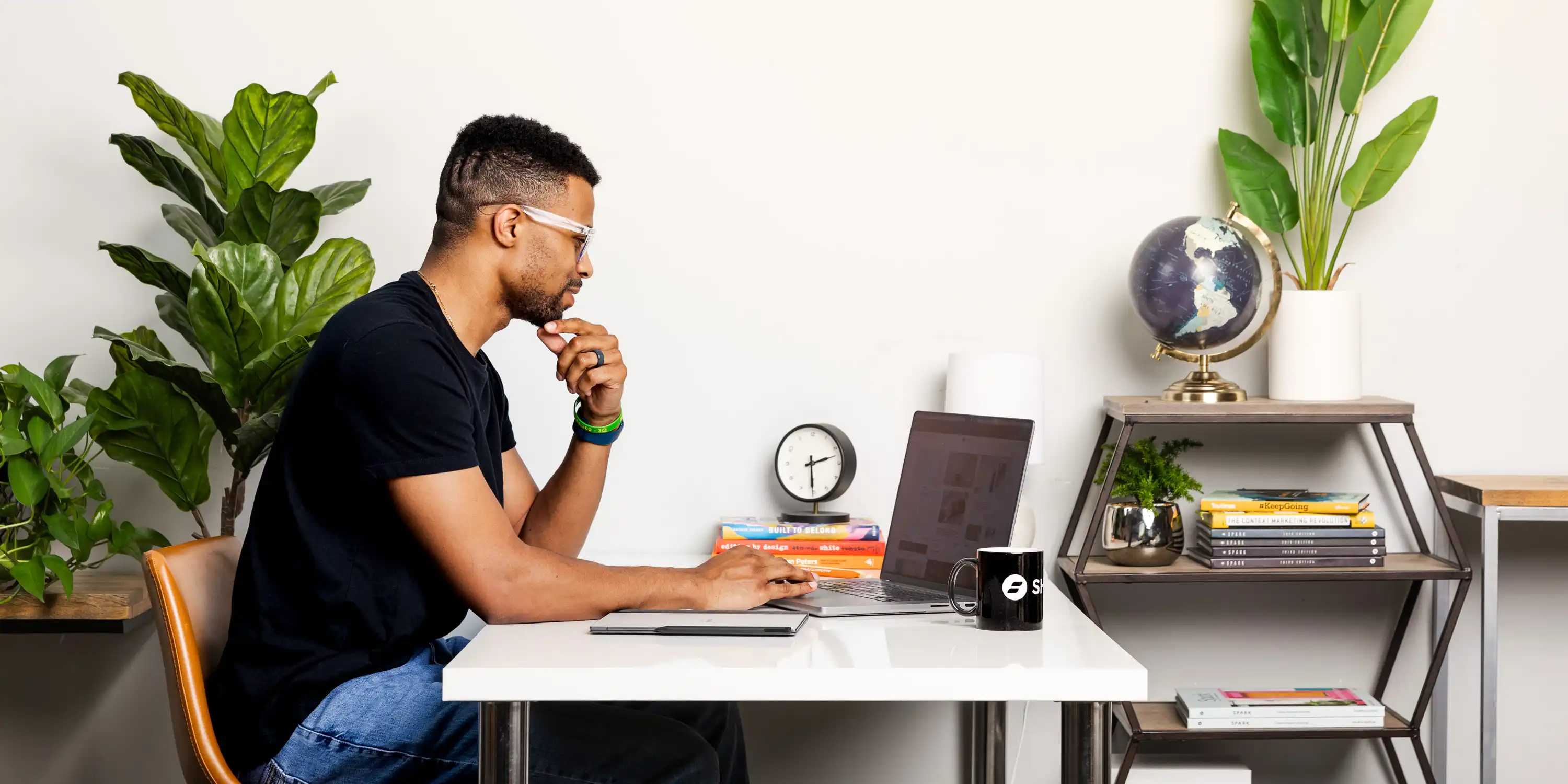 Focused man working at a desk with a laptop, surrounded by books, greenery, and a globe, symbolizing productivity and a strategic approach to learning how to attract students to your course.