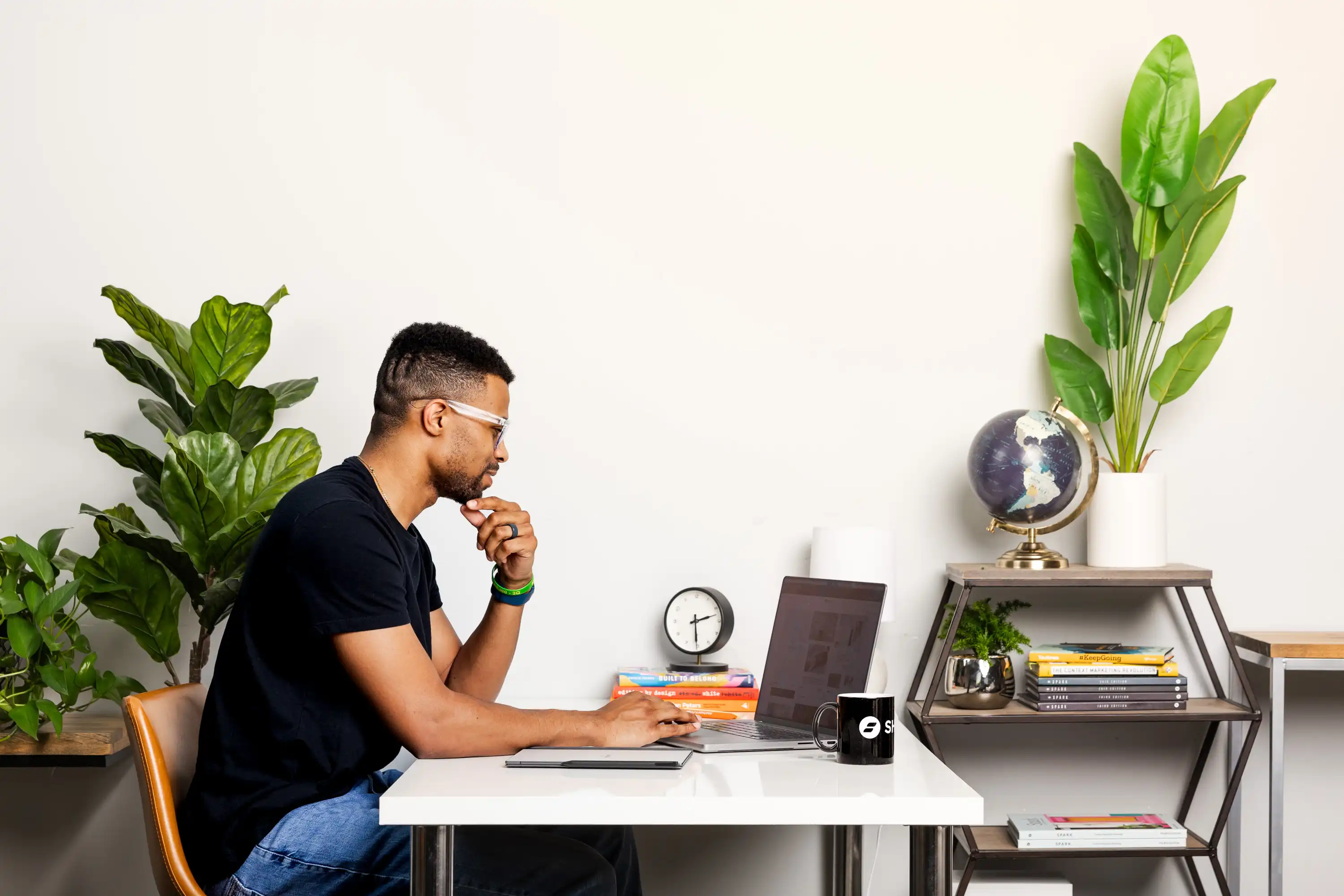 Focused man working at a desk with a laptop, surrounded by books, greenery, and a globe, symbolizing productivity and a strategic approach to learning how to attract students to your course.