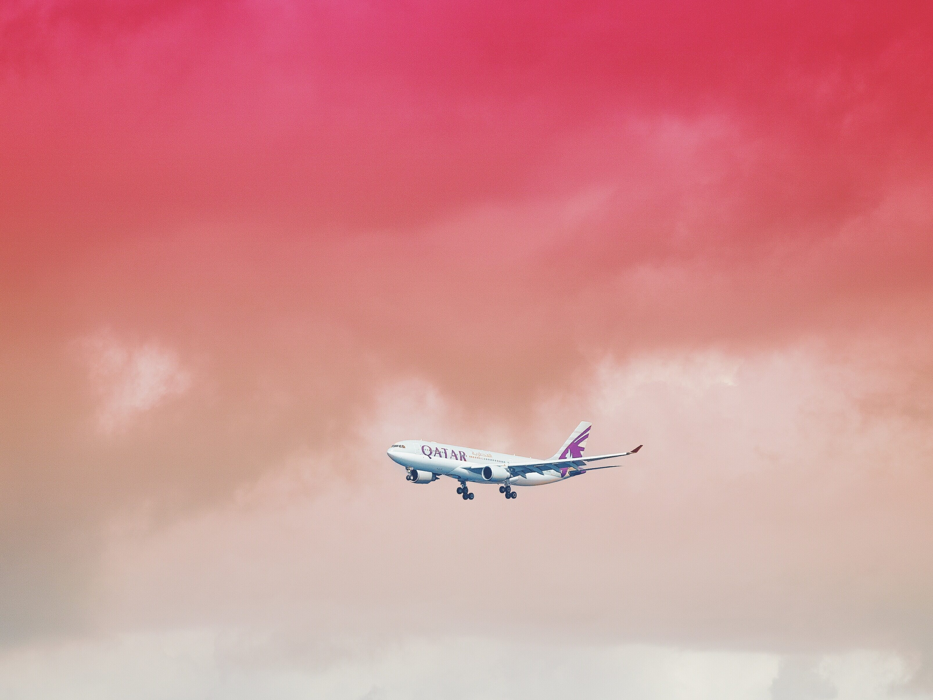 Qatar Airways passenger jet in flight against a pink-orange sunset sky with clouds.