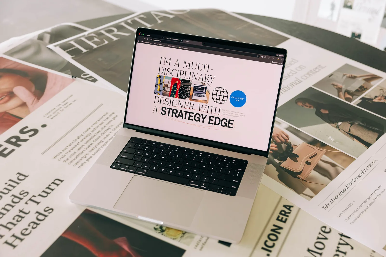Laptop displaying a Showit portfolio website homepage with the headline 'I'm a multi-disciplinary designer with a strategy edge,' surrounded by fashion magazines on a desk