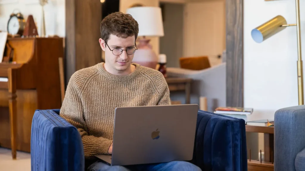 showit-website-builder-creative-entrepreneur-support - Showit Creative entrepreneur working on a laptop from a cozy armchair at home, building a business with the support Showit offers